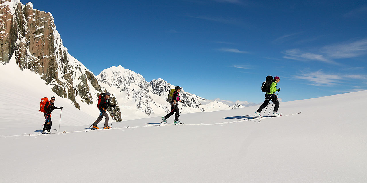 Ski tourers approaching the summit of Mount von Bulow in front of Mount Tasman